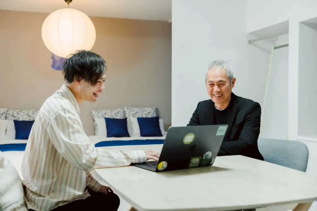 民泊を管理する笑顔のオーナーと担当者がおしゃれな内装の室内でPCを操作しながら交流する